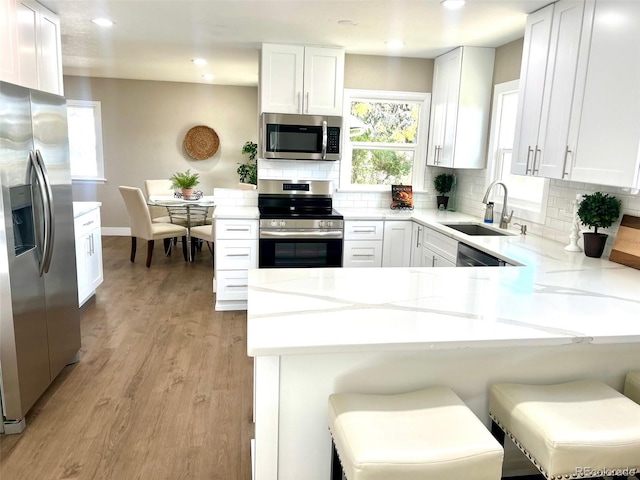 kitchen featuring kitchen peninsula, appliances with stainless steel finishes, a breakfast bar, sink, and white cabinetry