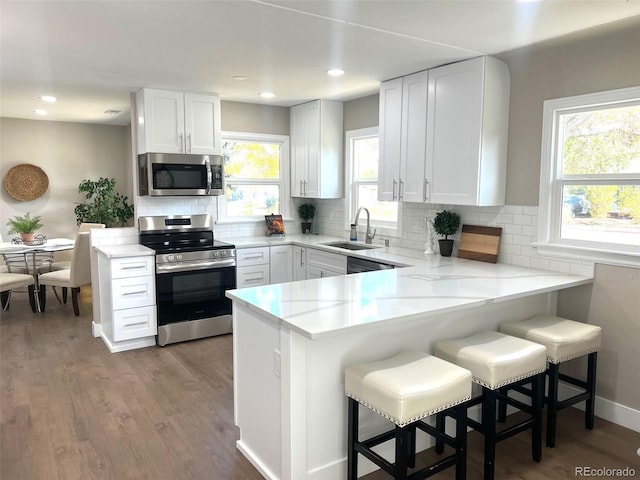 kitchen with kitchen peninsula, stainless steel appliances, white cabinetry, and a breakfast bar area