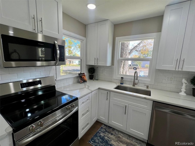 kitchen with sink, backsplash, stainless steel appliances, light stone countertops, and white cabinets