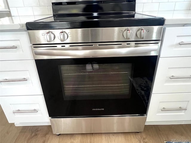 room details with white cabinetry, stainless steel stove, and light hardwood / wood-style floors