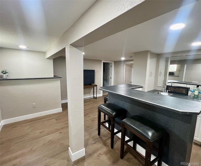 kitchen with a kitchen breakfast bar, sink, white cabinets, and light wood-type flooring