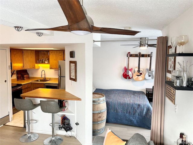 interior space with sink, a textured ceiling, light hardwood / wood-style flooring, range with electric stovetop, and stainless steel fridge