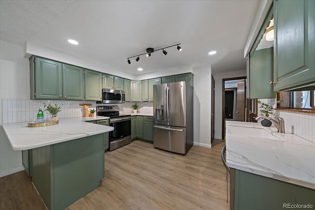 2130 Squires St, Longmont, CO 80501 - kitchen featuring stainless steel appliances, green cabinets, a peninsula, decorative backsplash, and light wood-style floors