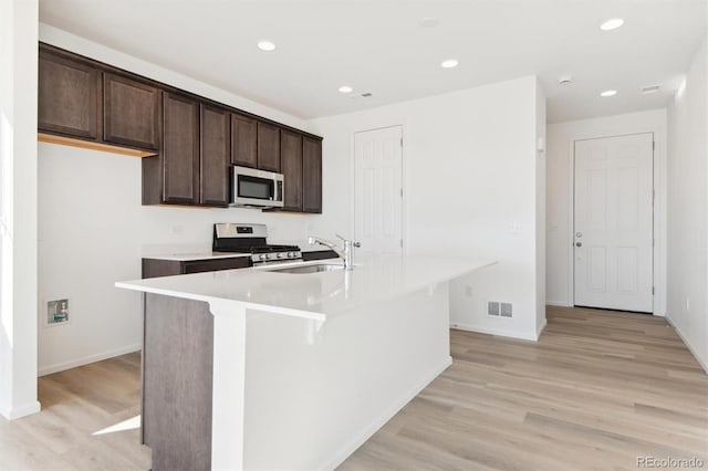 kitchen featuring appliances with stainless steel finishes, sink, light hardwood / wood-style flooring, and an island with sink