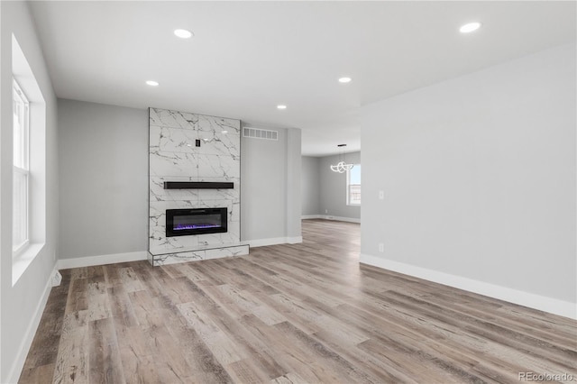 unfurnished living room with light wood-type flooring, a chandelier, and a high end fireplace