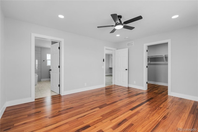 unfurnished bedroom featuring ensuite bath, ceiling fan, light hardwood / wood-style floors, a walk in closet, and a closet