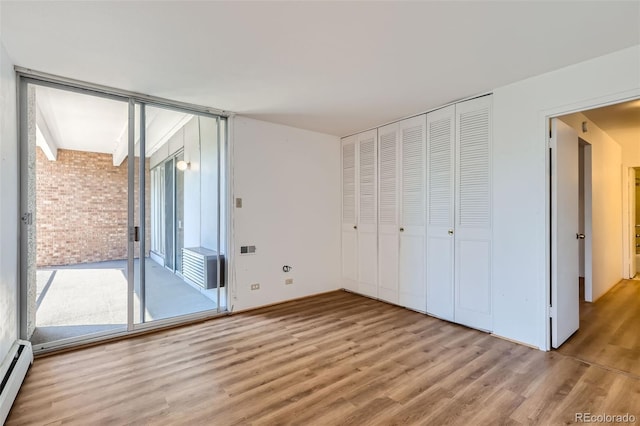 unfurnished bedroom with brick wall, a baseboard radiator, a closet, access to exterior, and hardwood / wood-style flooring