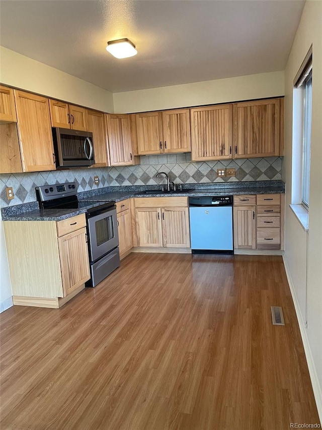 kitchen featuring sink, dark stone countertops, backsplash, hardwood / wood-style floors, and stainless steel appliances