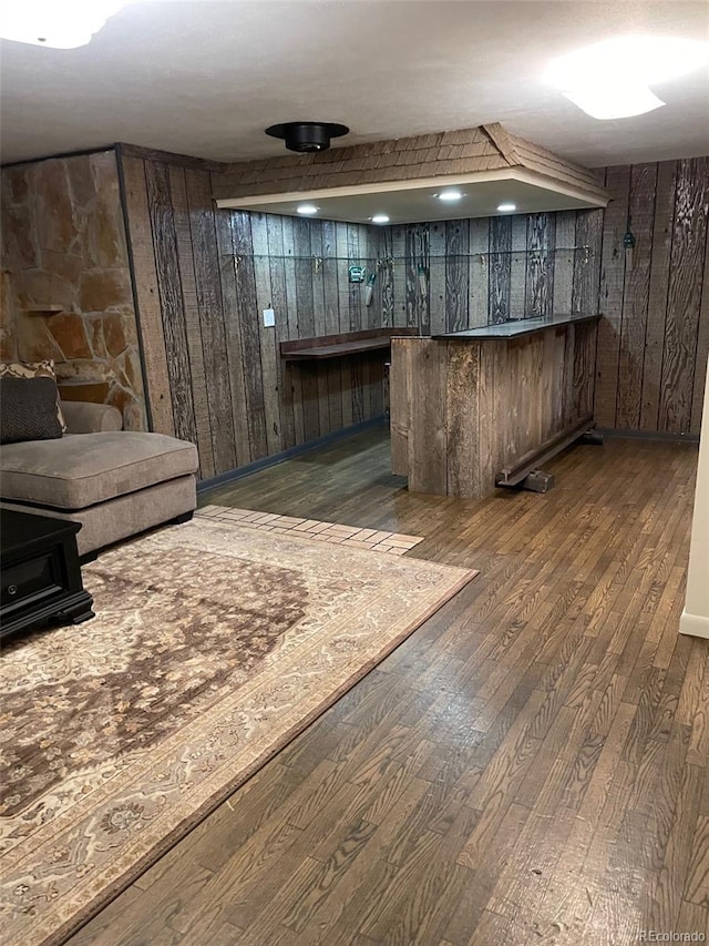 basement featuring wooden walls, indoor bar, and dark hardwood / wood-style flooring