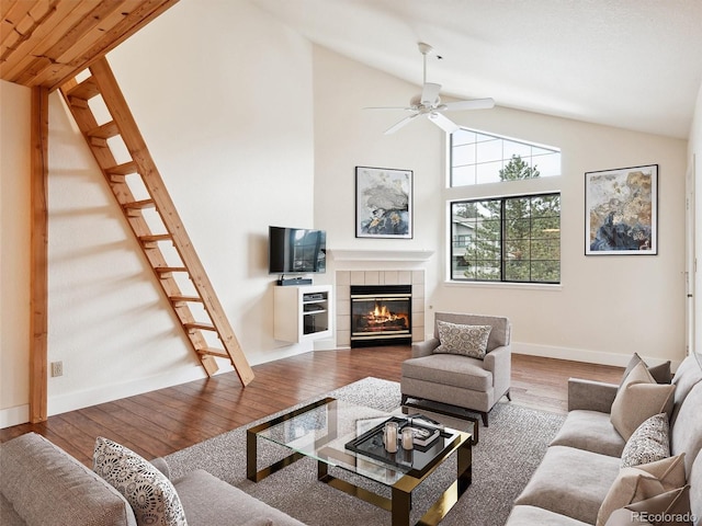 living room with a tile fireplace, wood-type flooring, high vaulted ceiling, and ceiling fan