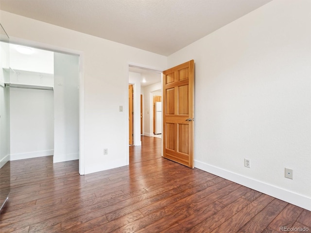 unfurnished bedroom featuring white refrigerator, dark hardwood / wood-style flooring, and a closet