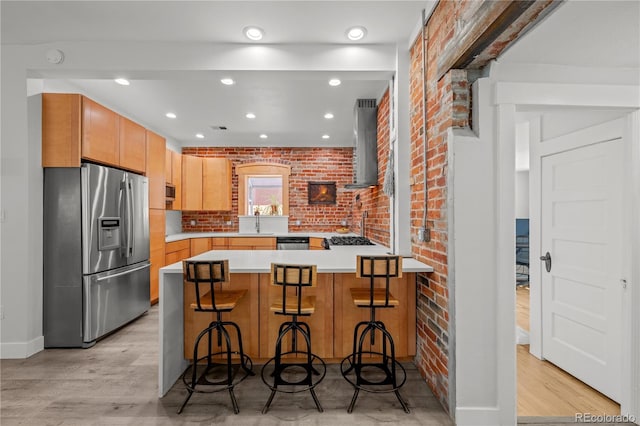 kitchen with stainless steel appliances, wall chimney range hood, light wood-style floors, a peninsula, and light countertops