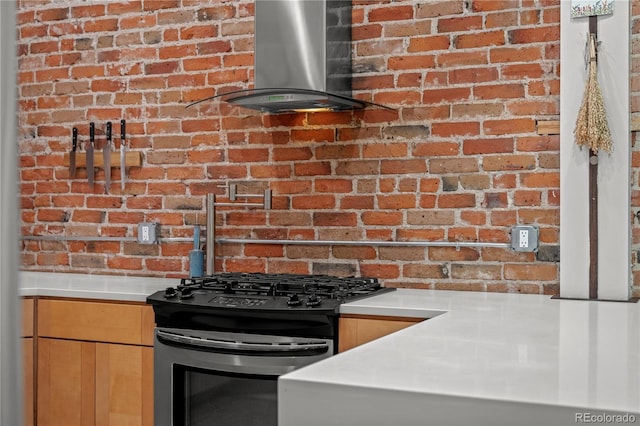 kitchen with wall chimney range hood, gas stove, brick wall, and light countertops