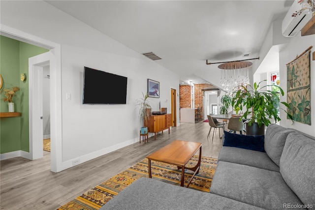 living area featuring an AC wall unit, a chandelier, wood finished floors, and baseboards