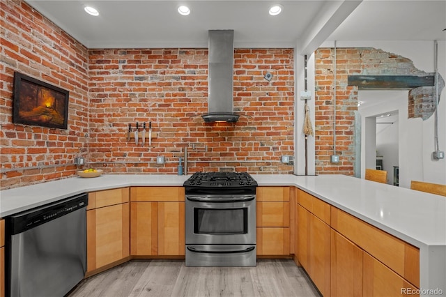 kitchen featuring appliances with stainless steel finishes, a peninsula, brick wall, wall chimney range hood, and light countertops