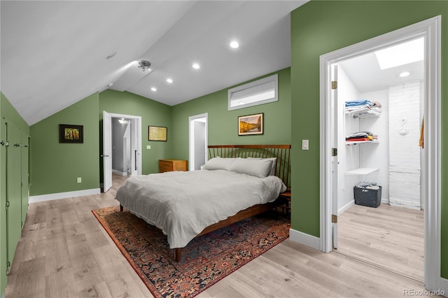 bedroom featuring vaulted ceiling, light wood finished floors, a spacious closet, baseboards, and a skylight