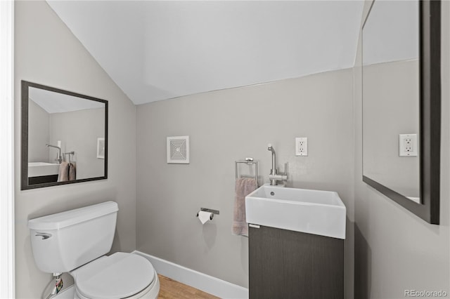 bathroom with lofted ceiling, toilet, vanity, wood finished floors, and baseboards