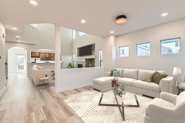 living area featuring light wood finished floors, baseboards, arched walkways, a fireplace, and recessed lighting