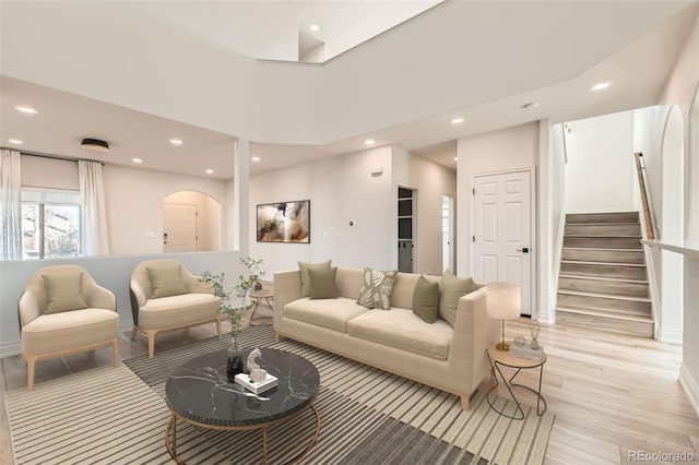 living room featuring arched walkways, stairway, light wood-style flooring, and recessed lighting