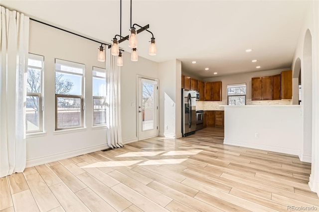 unfurnished living room featuring baseboards, light wood-type flooring, arched walkways, and recessed lighting