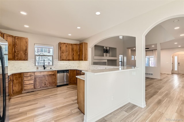 kitchen featuring light wood finished floors, appliances with stainless steel finishes, brown cabinetry, and a sink