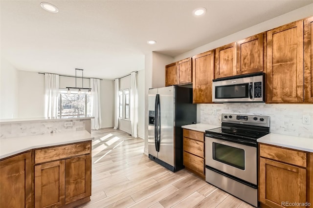 kitchen with stainless steel appliances, light countertops, decorative backsplash, brown cabinets, and light wood finished floors