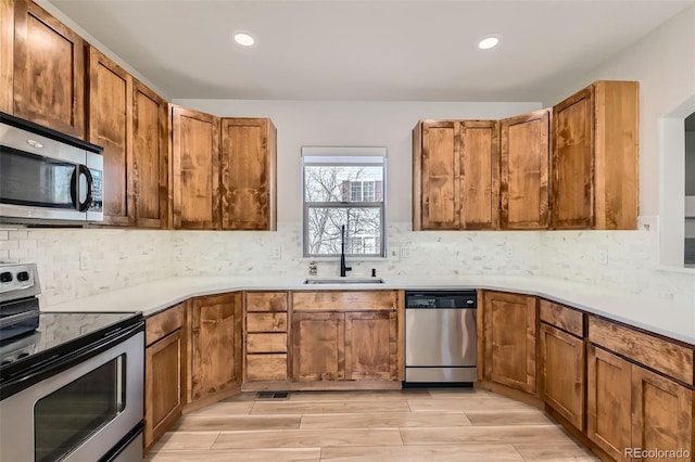 kitchen with brown cabinets, decorative backsplash, stainless steel appliances, and a sink