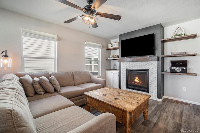 living room with a tiled fireplace, a textured ceiling, dark wood-type flooring, and ceiling fan