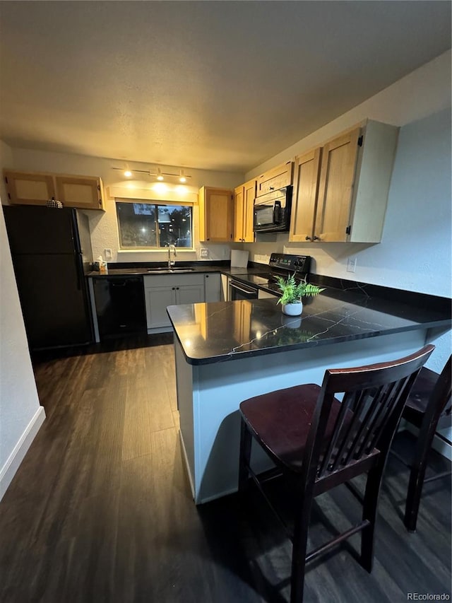 kitchen featuring sink, kitchen peninsula, dark wood-type flooring, black appliances, and a kitchen bar