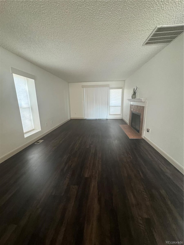 unfurnished living room with a tiled fireplace, a textured ceiling, and dark hardwood / wood-style flooring