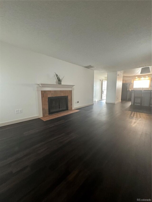 unfurnished living room featuring a textured ceiling, a tiled fireplace, and dark wood-type flooring