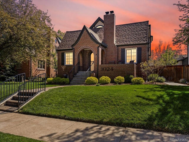 tudor home featuring brick siding, a lawn, and a chimney