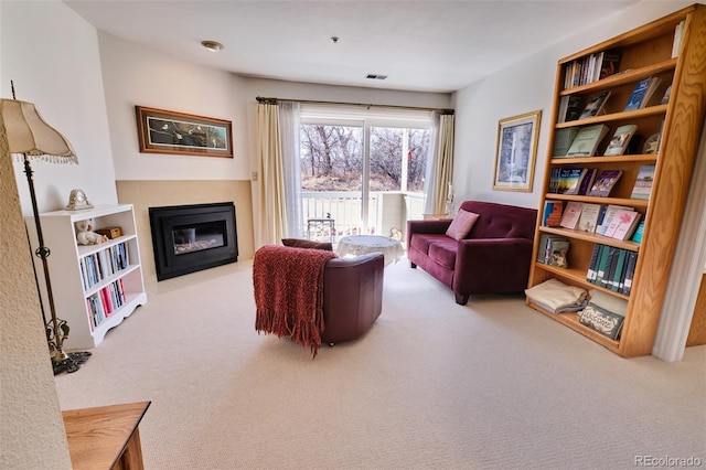 living area featuring carpet flooring, a glass covered fireplace, and visible vents