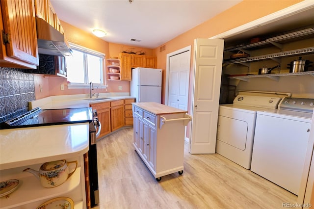 kitchen featuring washing machine and clothes dryer, open shelves, freestanding refrigerator, a sink, and under cabinet range hood