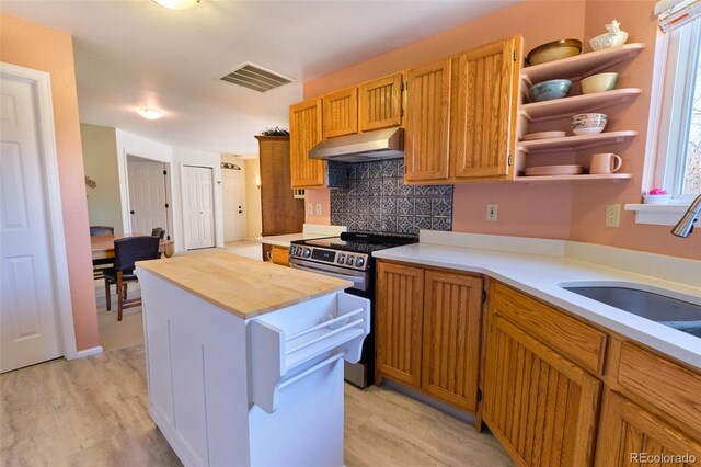 kitchen with under cabinet range hood, wood counters, a kitchen island, visible vents, and stainless steel electric stove