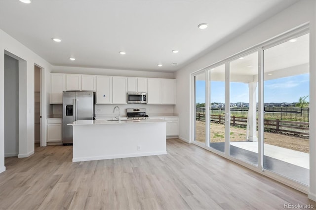 kitchen with an island with sink, stainless steel appliances, white cabinetry, and light wood-type flooring