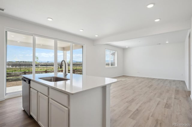 kitchen with light countertops, light wood-style flooring, a sink, a center island with sink, and dishwasher