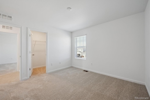 unfurnished bedroom with a spacious closet, carpet flooring, and visible vents