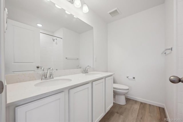 bathroom with double vanity, toilet, wood finished floors, and a sink