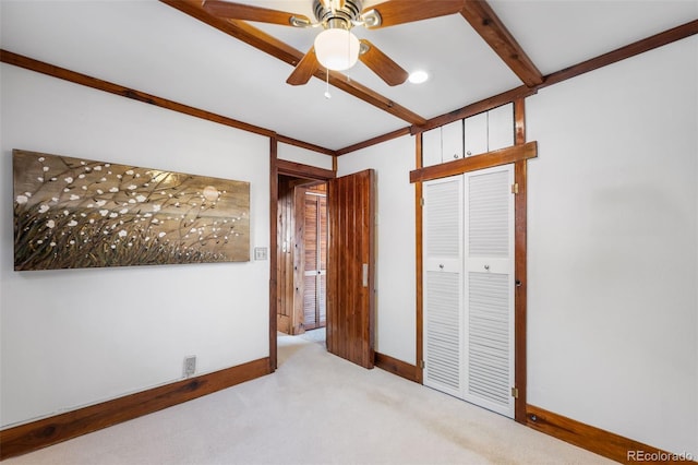 unfurnished bedroom featuring light colored carpet, a ceiling fan, baseboards, a closet, and beamed ceiling