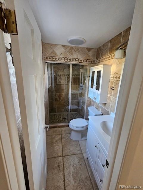 bathroom with tile walls, vanity, toilet, and a shower with door