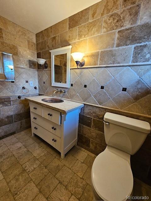 bathroom featuring vanity, tile walls, and toilet