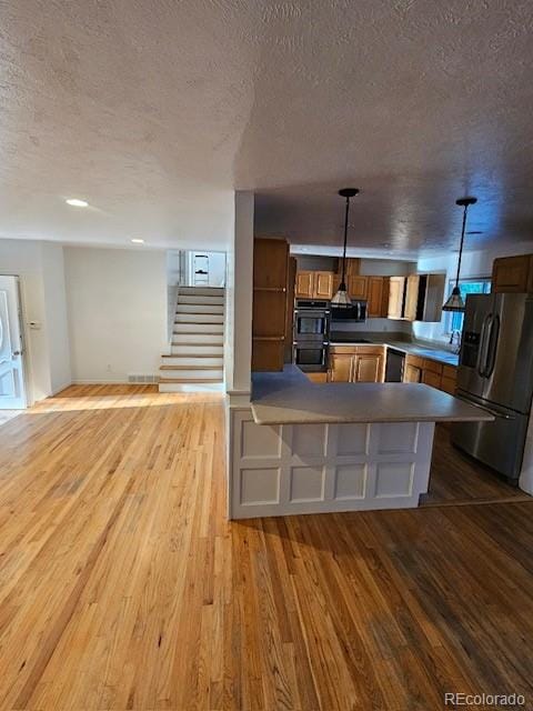 kitchen featuring wood-type flooring, decorative light fixtures, a textured ceiling, and appliances with stainless steel finishes