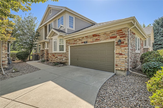 view of front of property featuring driveway, stone siding, an attached garage, and central AC