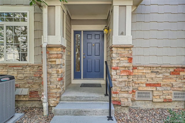 view of exterior entry featuring stone siding, central AC, visible vents, and crawl space