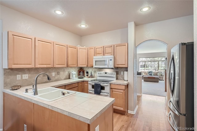 kitchen with light countertops, light brown cabinets, a sink, white appliances, and a peninsula