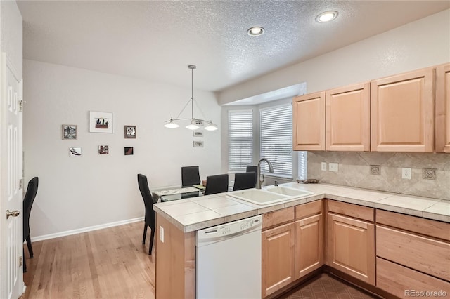 kitchen with white dishwasher, a peninsula, a sink, tasteful backsplash, and pendant lighting