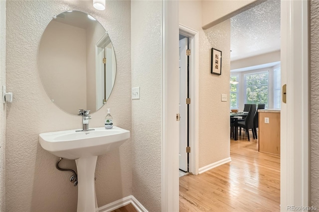 bathroom with a textured wall, wood finished floors, and baseboards