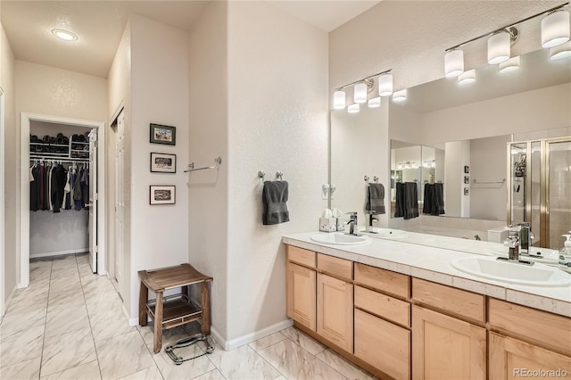 bathroom with a walk in closet, marble finish floor, a sink, and double vanity