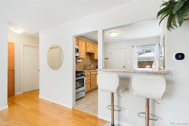 kitchen with a breakfast bar area, light hardwood / wood-style flooring, decorative backsplash, kitchen peninsula, and stainless steel appliances